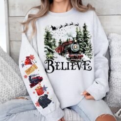 Black Christmas sweatshirt featuring a vintage train in a snowy forest with the word Believe, and Polar Express themed sleeve prints like a golden ticket and hot cocoa