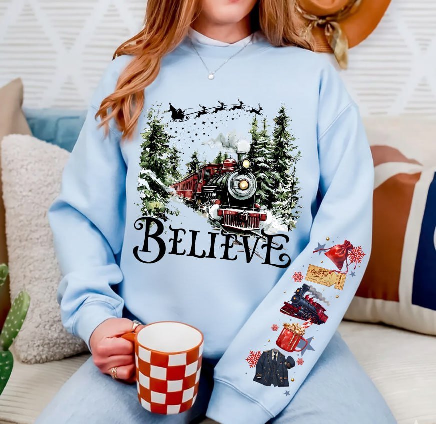 Black Christmas sweatshirt featuring a vintage train in a snowy forest with the word Believe, and Polar Express themed sleeve prints like a golden ticket and hot cocoa