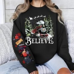 Black Christmas sweatshirt featuring a vintage train in a snowy forest with the word Believe, and Polar Express themed sleeve prints like a golden ticket and hot cocoa
