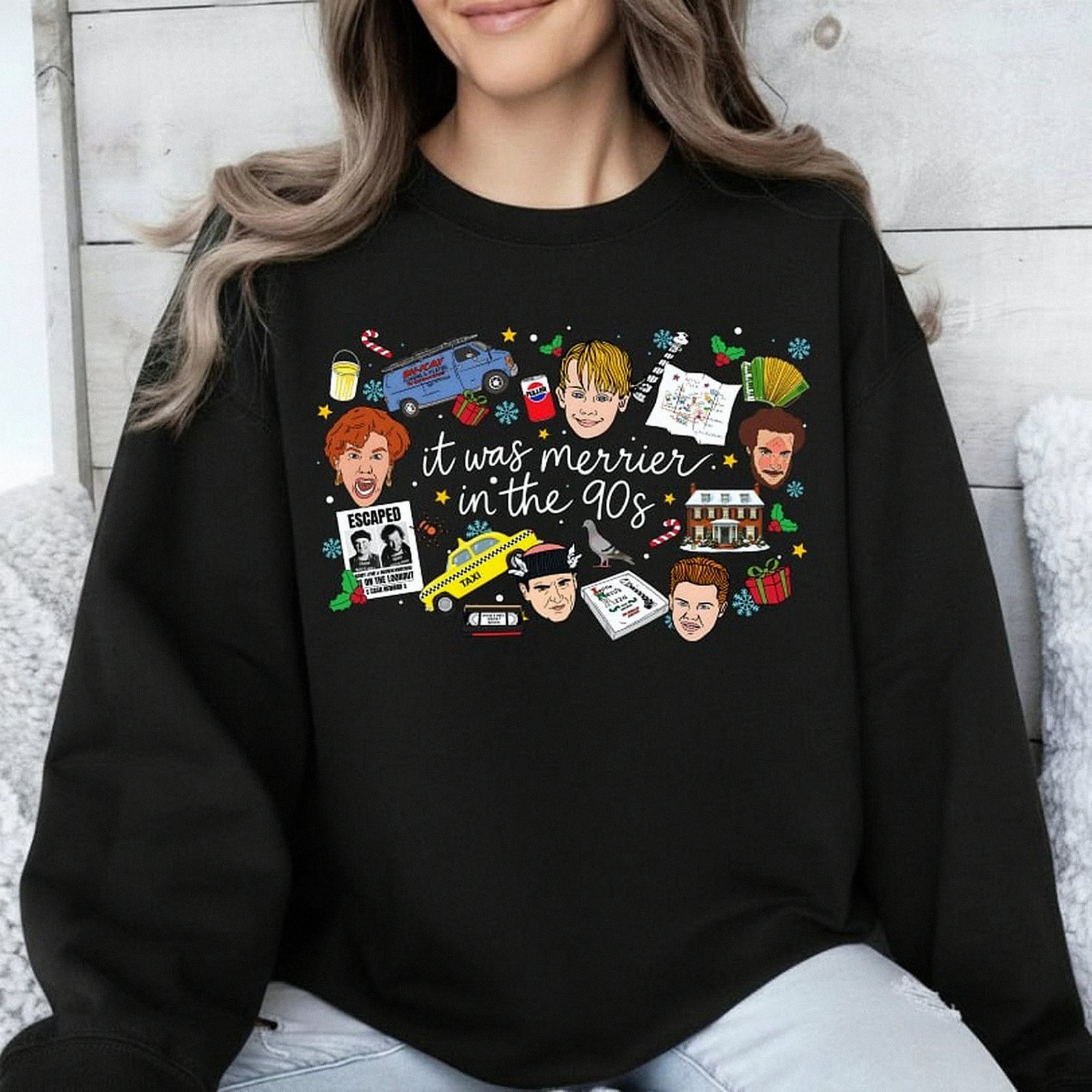 White crewneck Christmas sweatshirt featuring a retro 90s holiday movie collage design with the text "it was merrier in the 90s" alongside nostalgic characters and icons