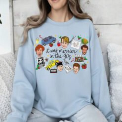 White crewneck Christmas sweatshirt featuring a retro 90s holiday movie collage design with the text "it was merrier in the 90s" alongside nostalgic characters and icons