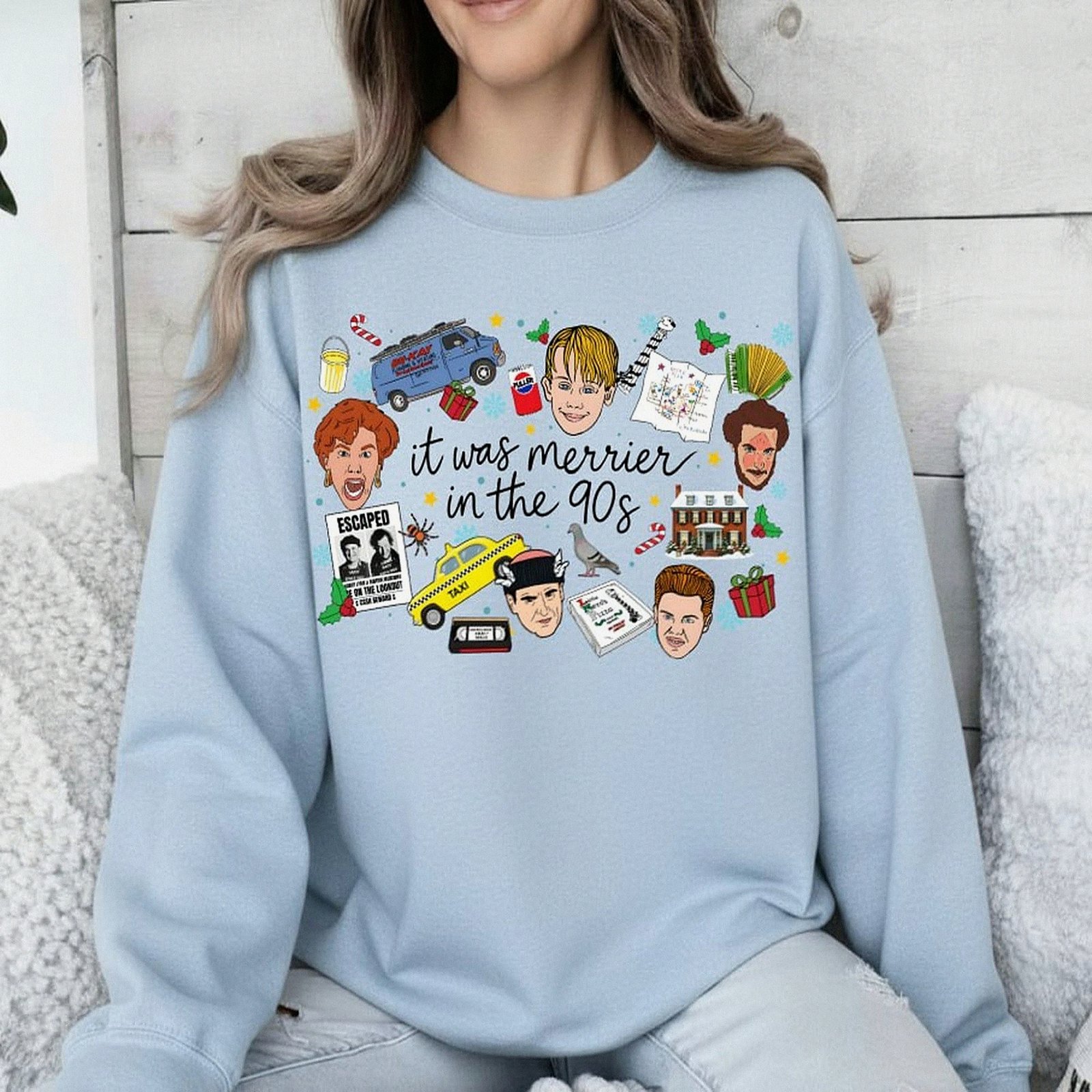 White crewneck Christmas sweatshirt featuring a retro 90s holiday movie collage design with the text "it was merrier in the 90s" alongside nostalgic characters and icons