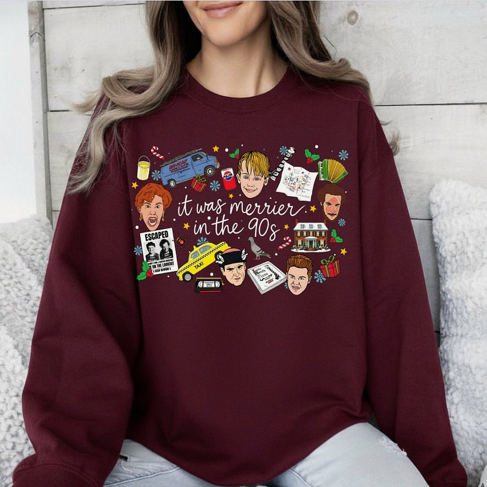 White crewneck Christmas sweatshirt featuring a retro 90s holiday movie collage design with the text "it was merrier in the 90s" alongside nostalgic characters and icons